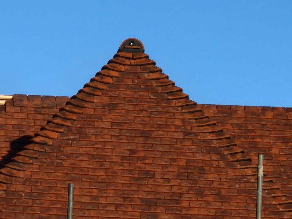 A brick roof designed in a triangular shape against a clear blue sky. The bricks are arranged in a stepped pattern with a decorative element at the peak. Two vertical poles are visible on either side of the roof.
